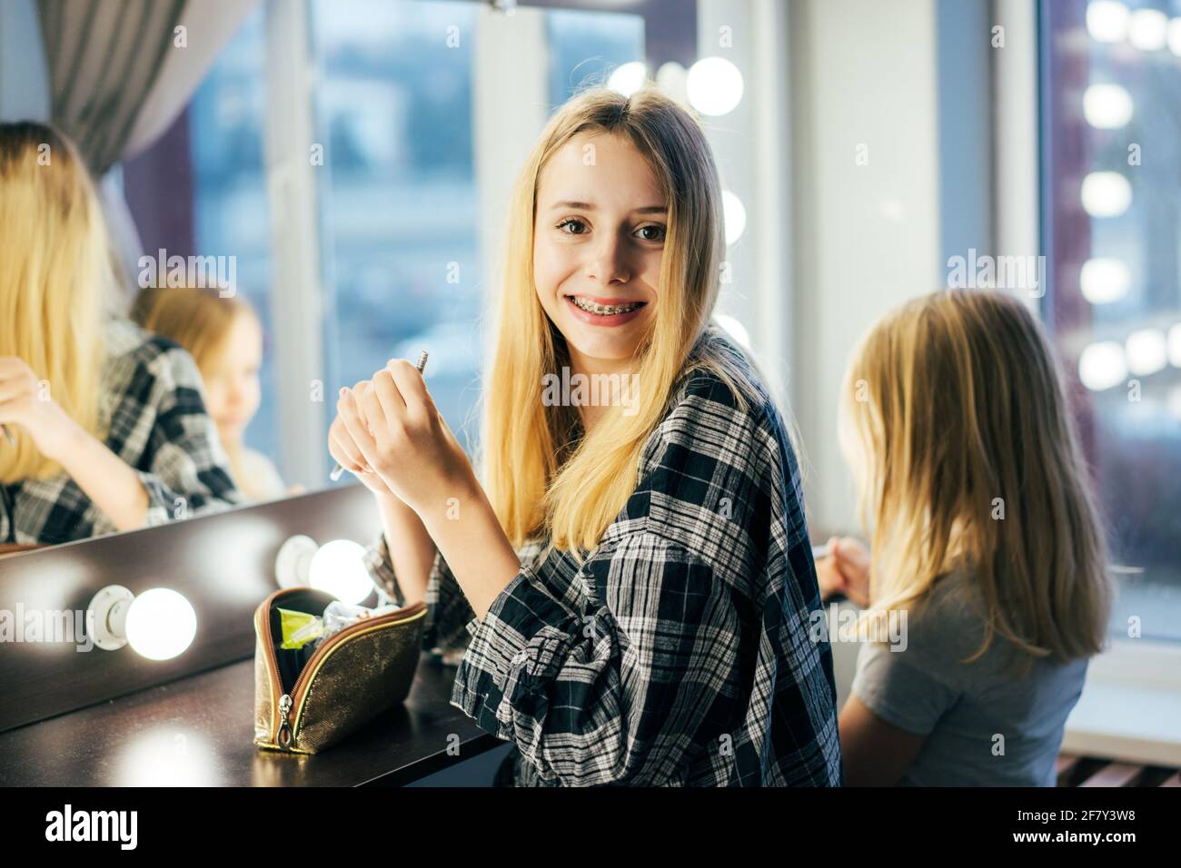 Life of a teenager, a girl with braces on her teeth smiles looking into the camera. Blonde girl in a shirt posing in front of the mirror in the dressi Stock Photo