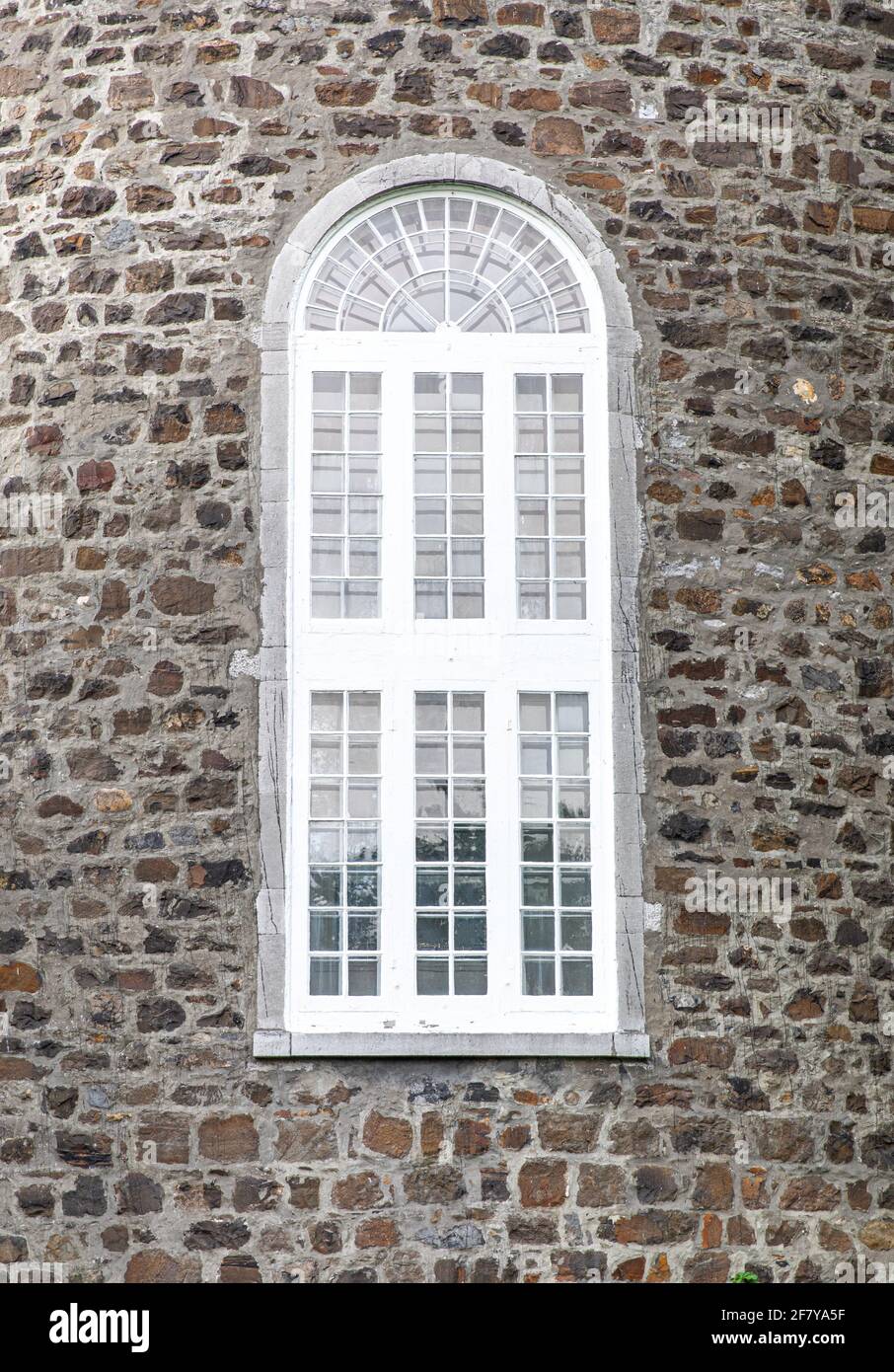 Tall window with arched top in the center of a stone wall Stock Photo