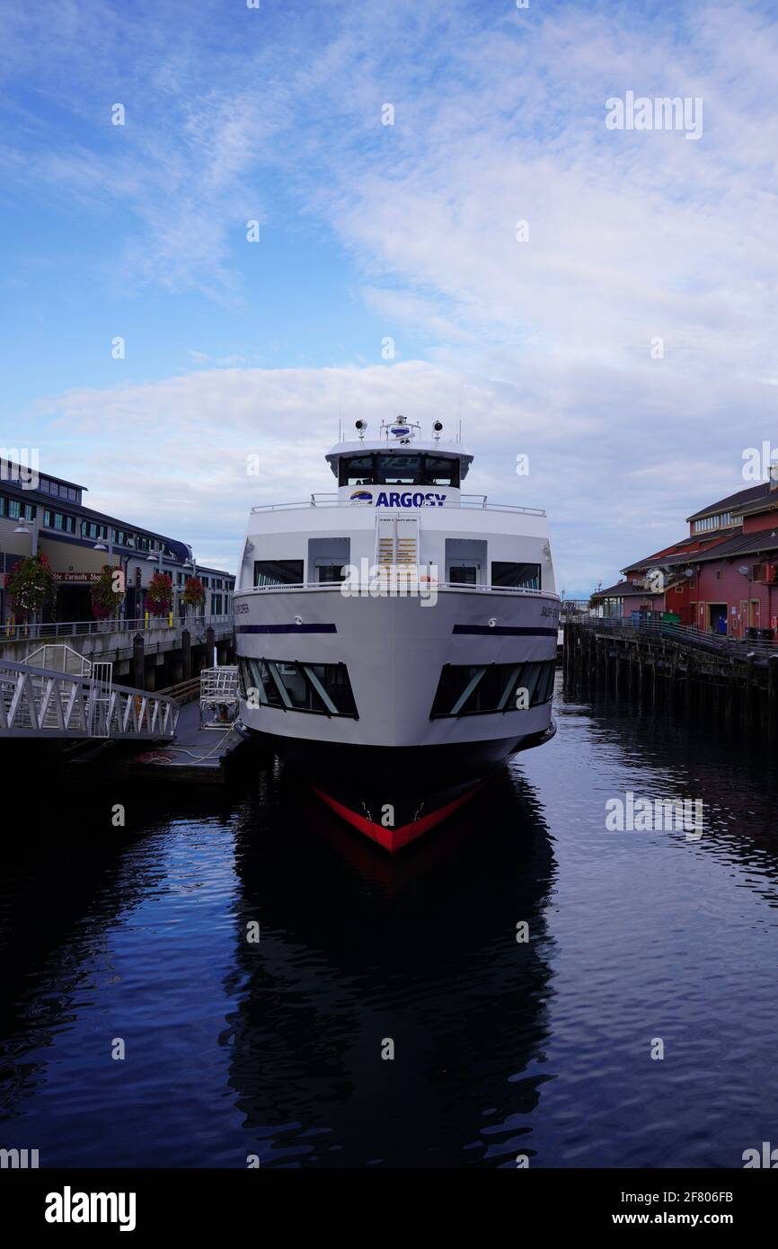 A cruises boat is docked on water at pier of Seattle, USA, with its reflection on ocean water. Stock Photo