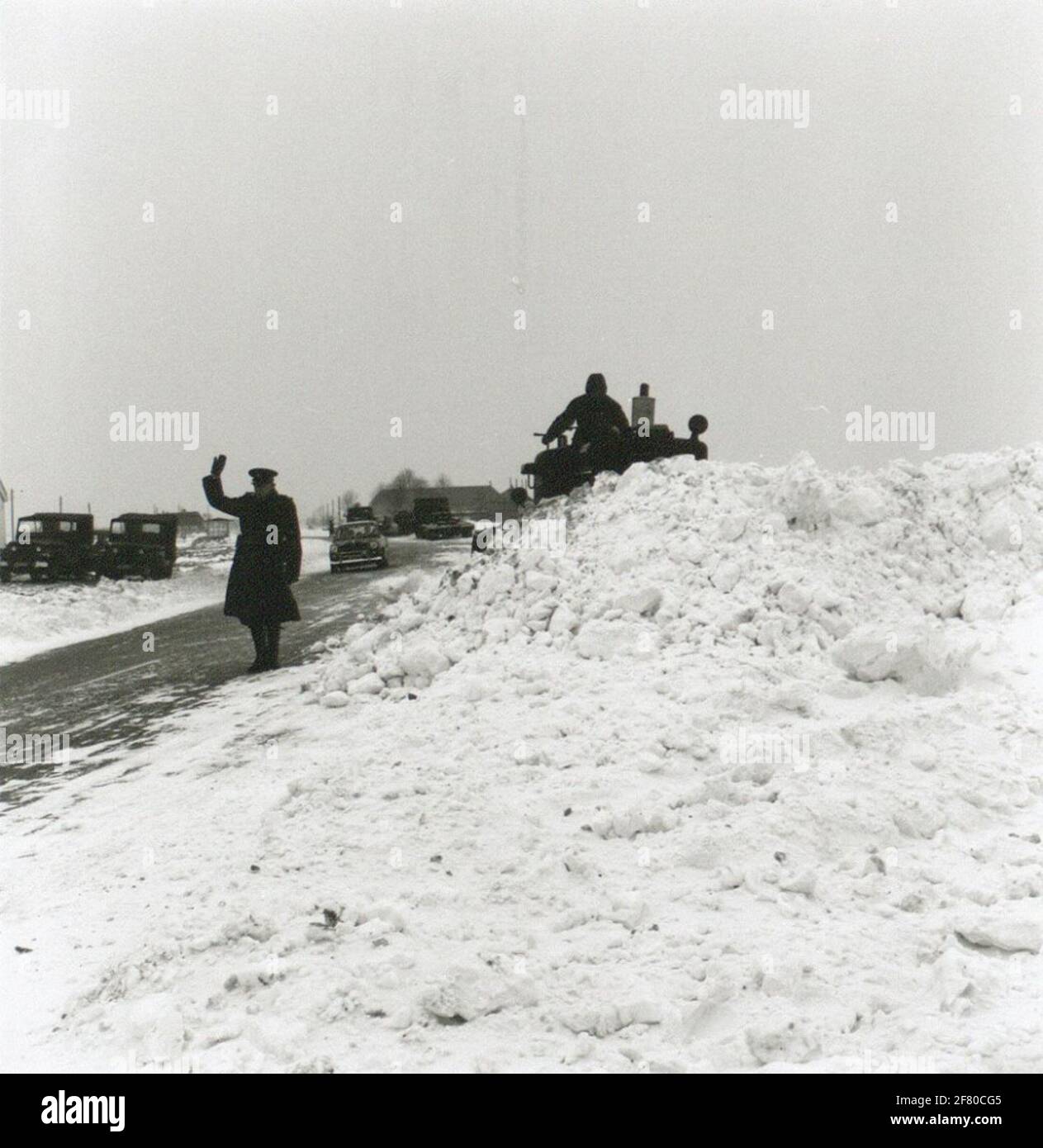 With a bulldozer, the genius makes snow-free in the area of Kampen and Zwolle during the strict winter from the beginning of 1963. A Marechaussee regulates traffic in the work. Stock Photo