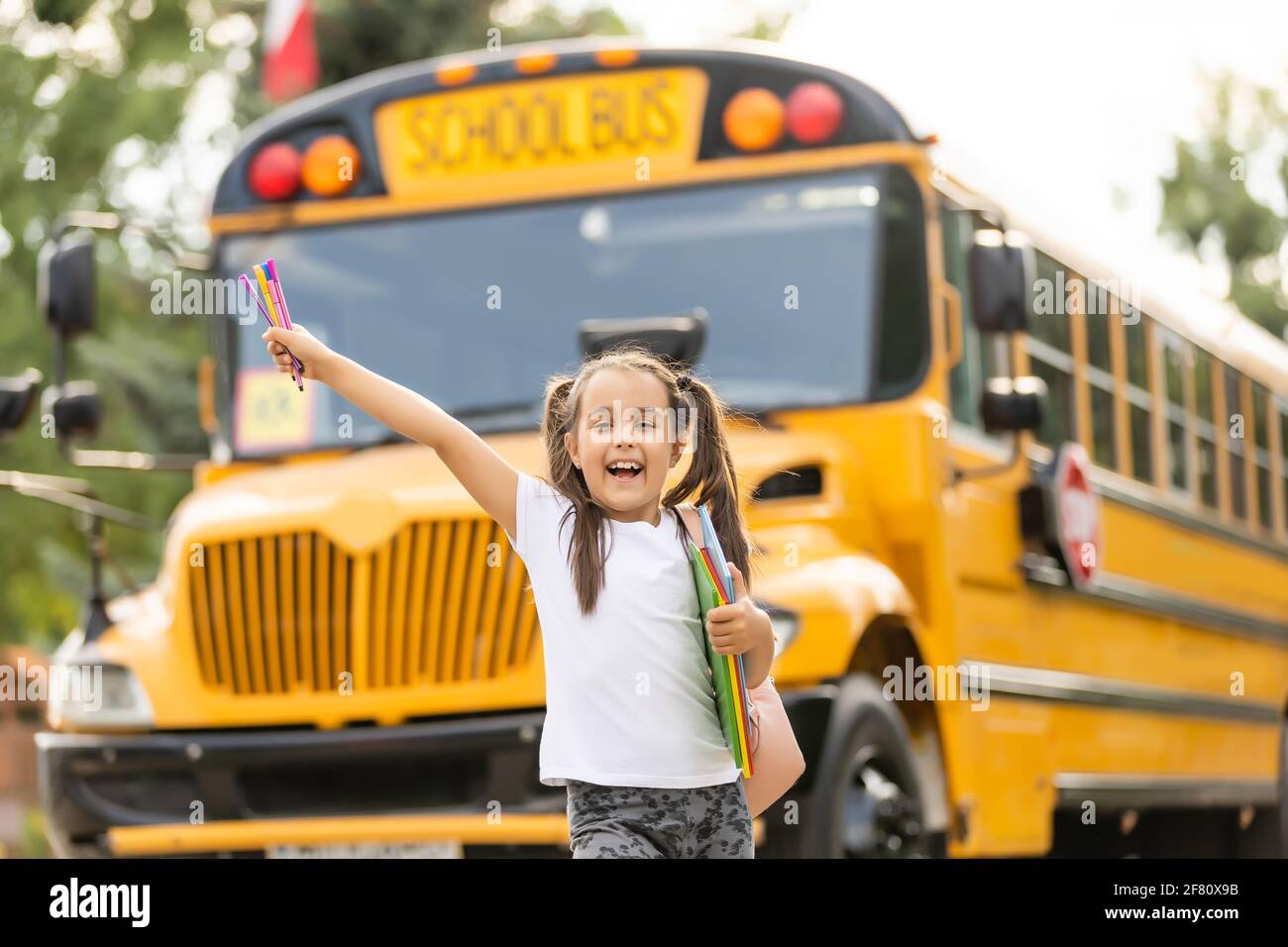 Cute girl with a backpack standing near bus going to school posing to