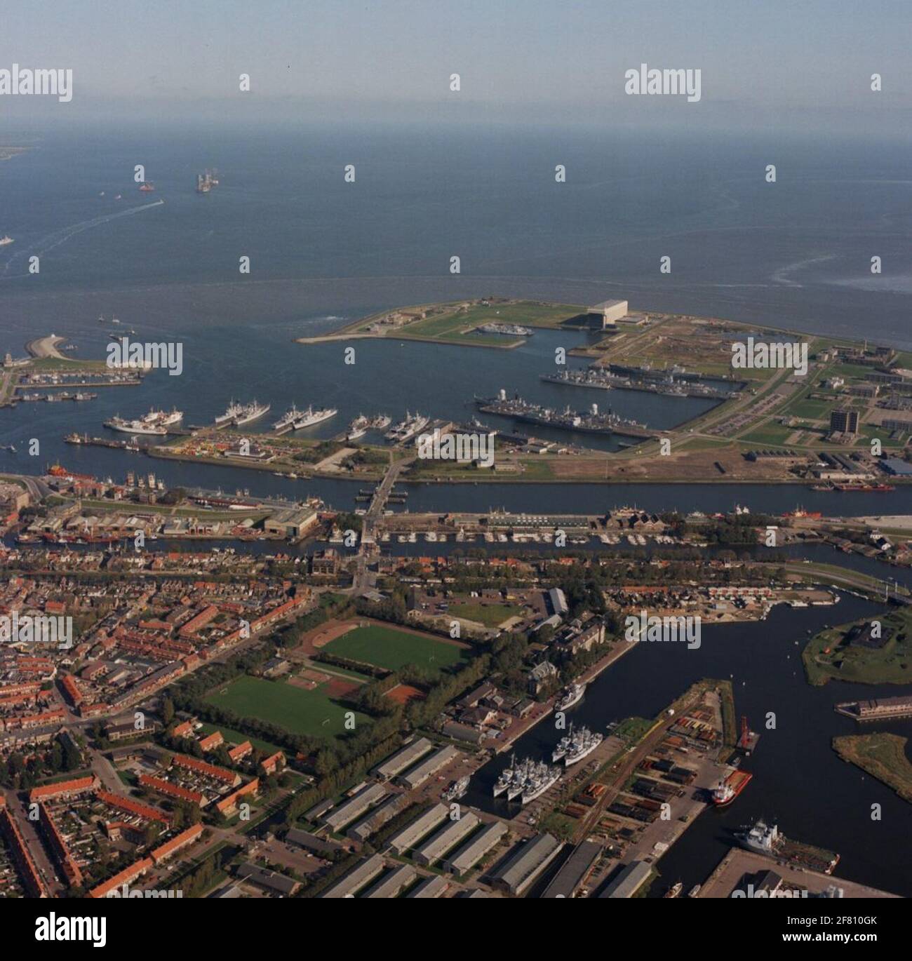 Aerial recording of Den Helder. In the new Marinehaven Den Helder, many warships lie inside, including the two guide arms of the tromp class (with bulb), Hr.Ms. De Ruyter (1976-2001) and Hr.Ms. Tromp (1975-1999). The supply ships Hr.Ms. Poolster (1964-1994) and Hr.Ms. Zuiderkruis (1975-2012). The rectangular building on the top of the harbor is the new covered dock of the national yard. On the lower part of the photo, the barracks of the Mining Service (MD) can be seen with a few mines' vessels in the inserts. In addition to the barracks of the MD the Marine Sportpark Ruyghweg. Stock Photo