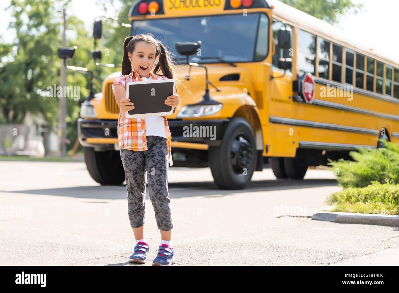 Little girl standing by a big school bus door with her backpack Stock