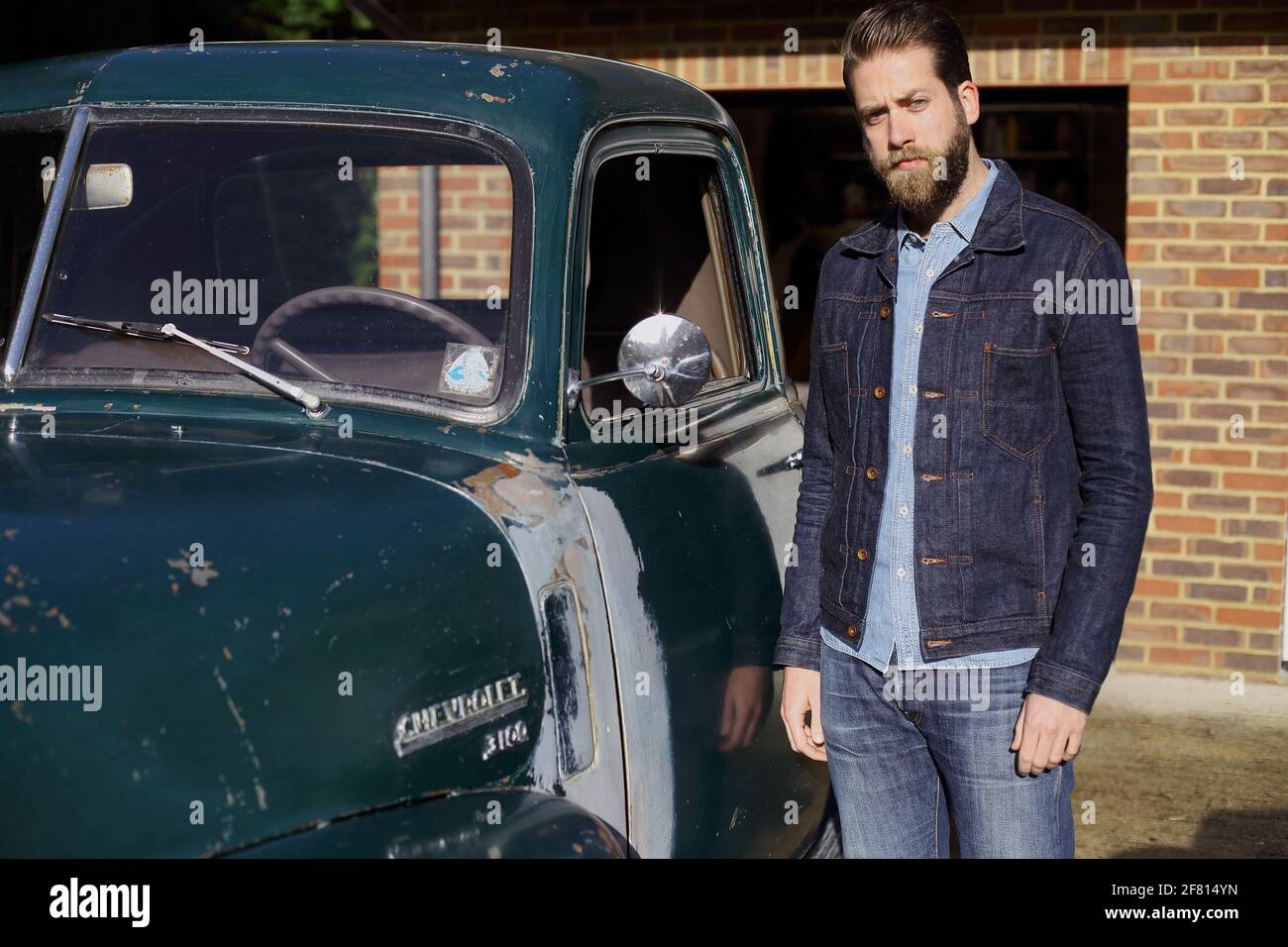 berded man wearing jeans standing next to pickup chevrolet classic car  outside . Stock Photo