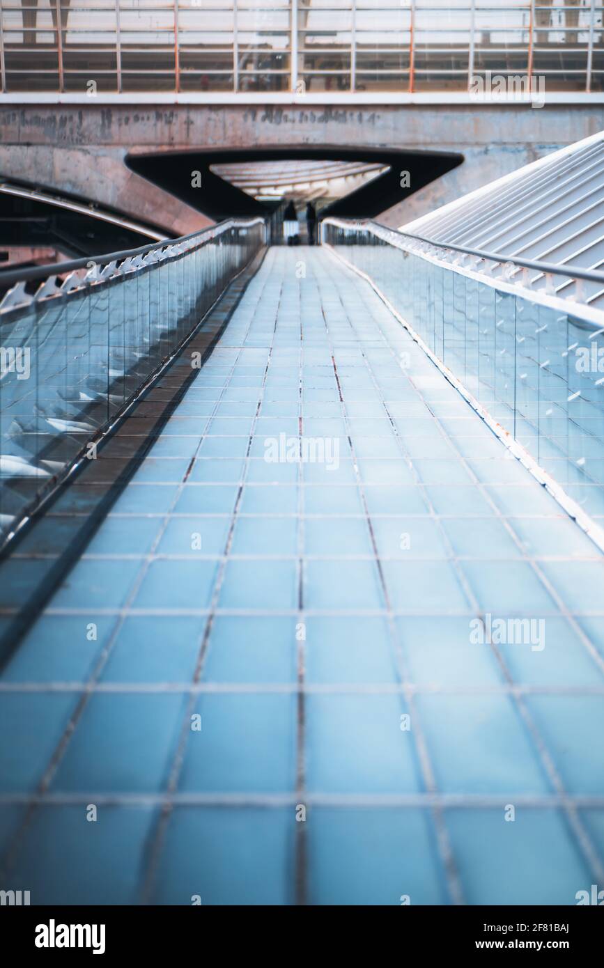 Vertical shot of a long modern overhead passage made of blue glass tiled blocks stretching into the distance with glass fence and chrome banister endi Stock Photo