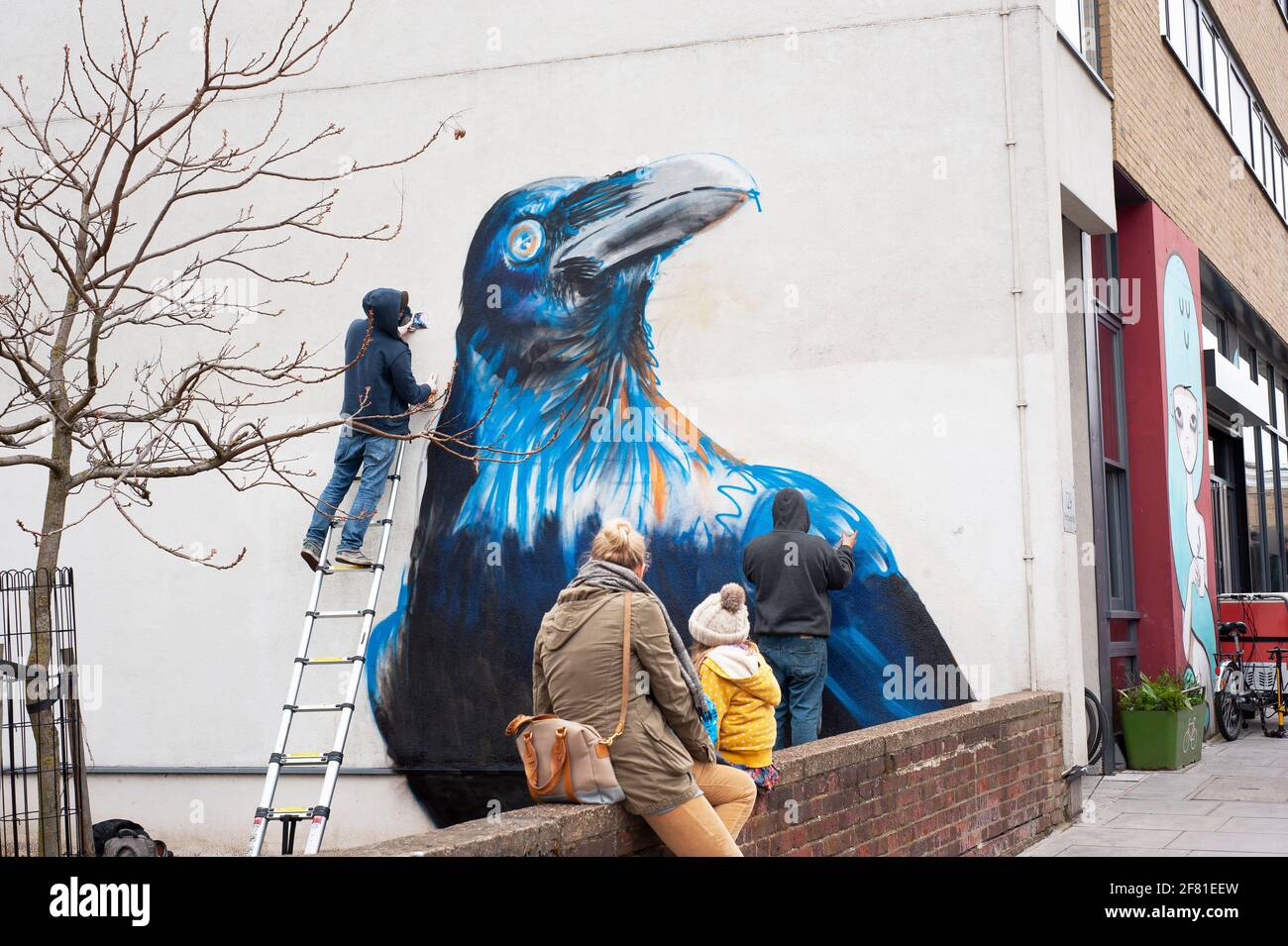 Street artists: Boe + Irony in action. Crow mural in the making on Whiston Road, E2 East London, UK. Apr 2013 Stock Photo