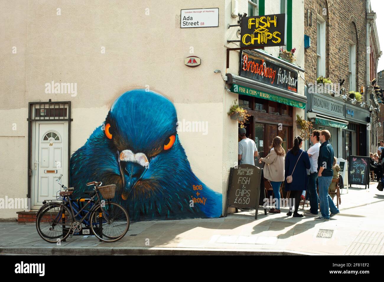 People lining up outside a Fish & chips shop on Broadway Market with a large pigeon (by Boe & Irony) watching around the corner. London, UK. Apr 2013 Stock Photo