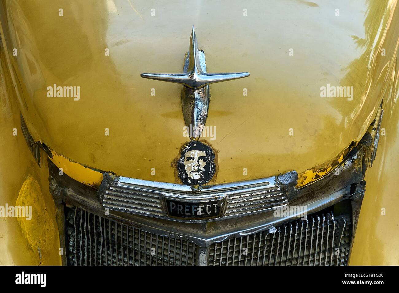 A Che Guevara car sticker placed under the silver hood ornament of a rusty old yellow Ford Prefect in Trinidad, Cuba Stock Photo