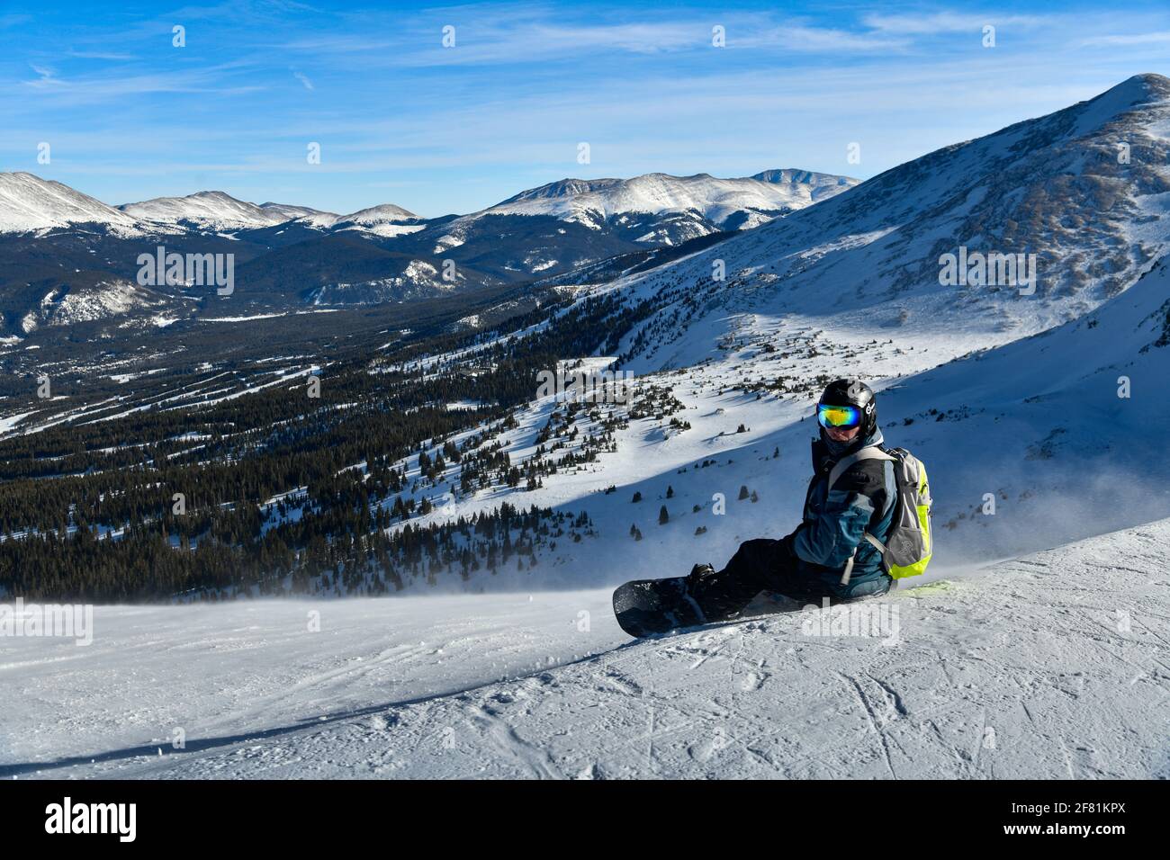 Snowboarder sitting on snowy hill and observing way down terrains. Extreme winter sports. Panoramic shot. Breckenridge, CO Stock Photo