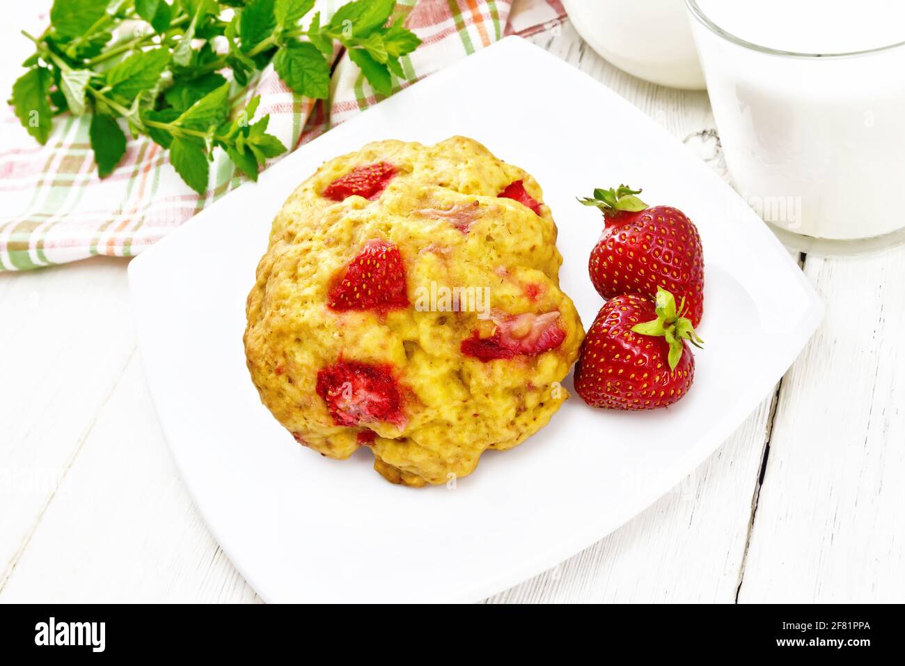 Strawberry scones in a plate with berries, a towel, mint, milk in jug and glass on wooden board background Stock Photo