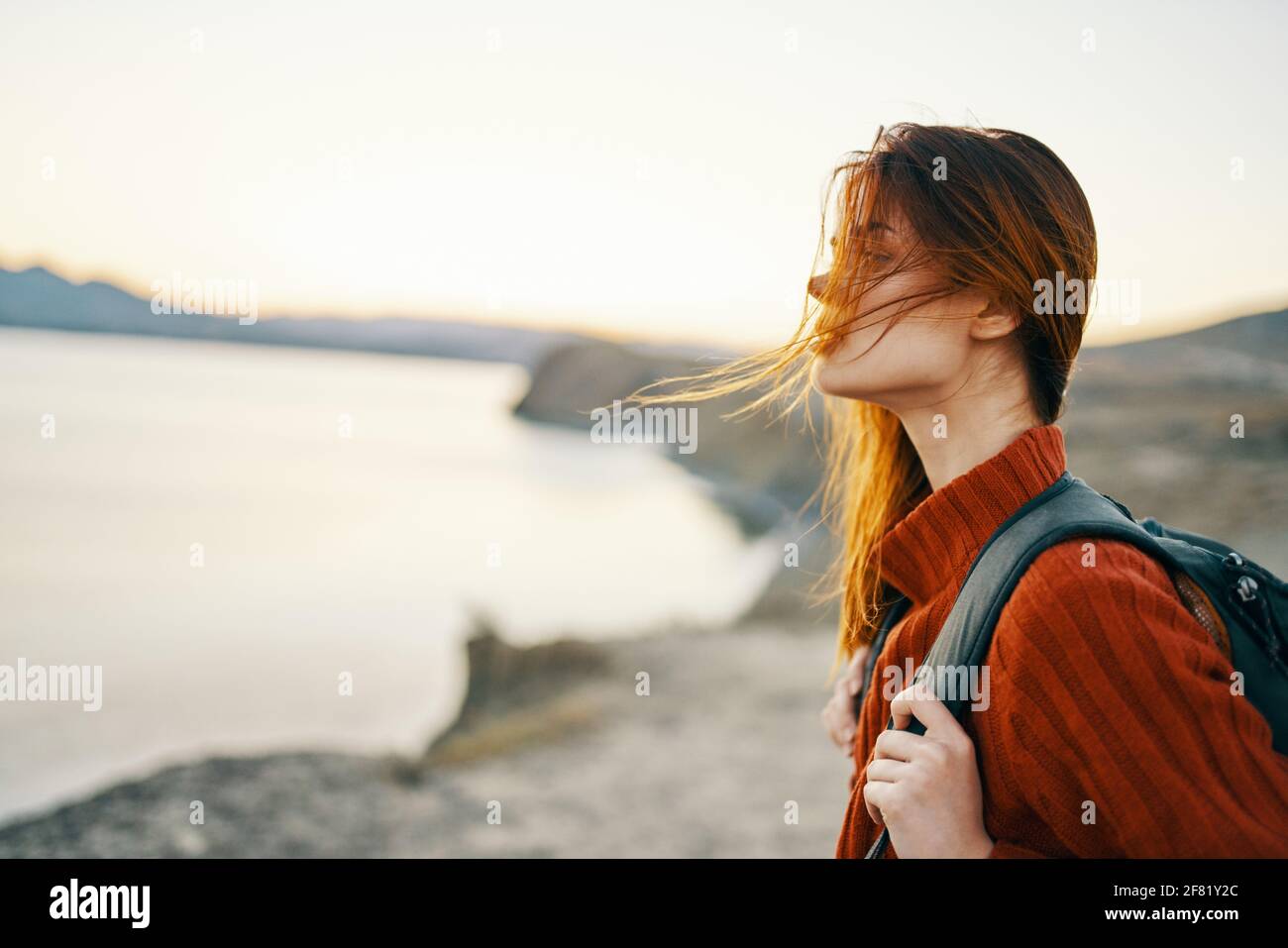 woman tourist in a sweater with a backpack in autumn in the mountains near the sea Stock Photo