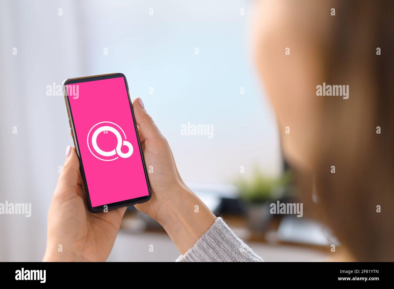 Kyiv, Ukraine - April 2, 2021: Google Fuchsia OS logo on the mobile phone screen. A woman is holding smartphone with Fuchsia logo on the display, operating system developed by Google Corporation Stock Photo