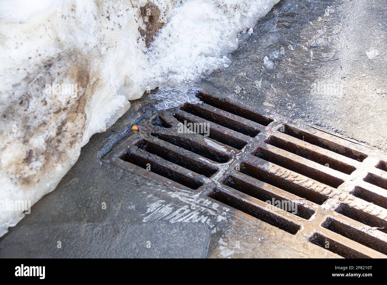 Water flows through the manhole cover, melting snow in the spring. View water flowing in sewage Stock Photo