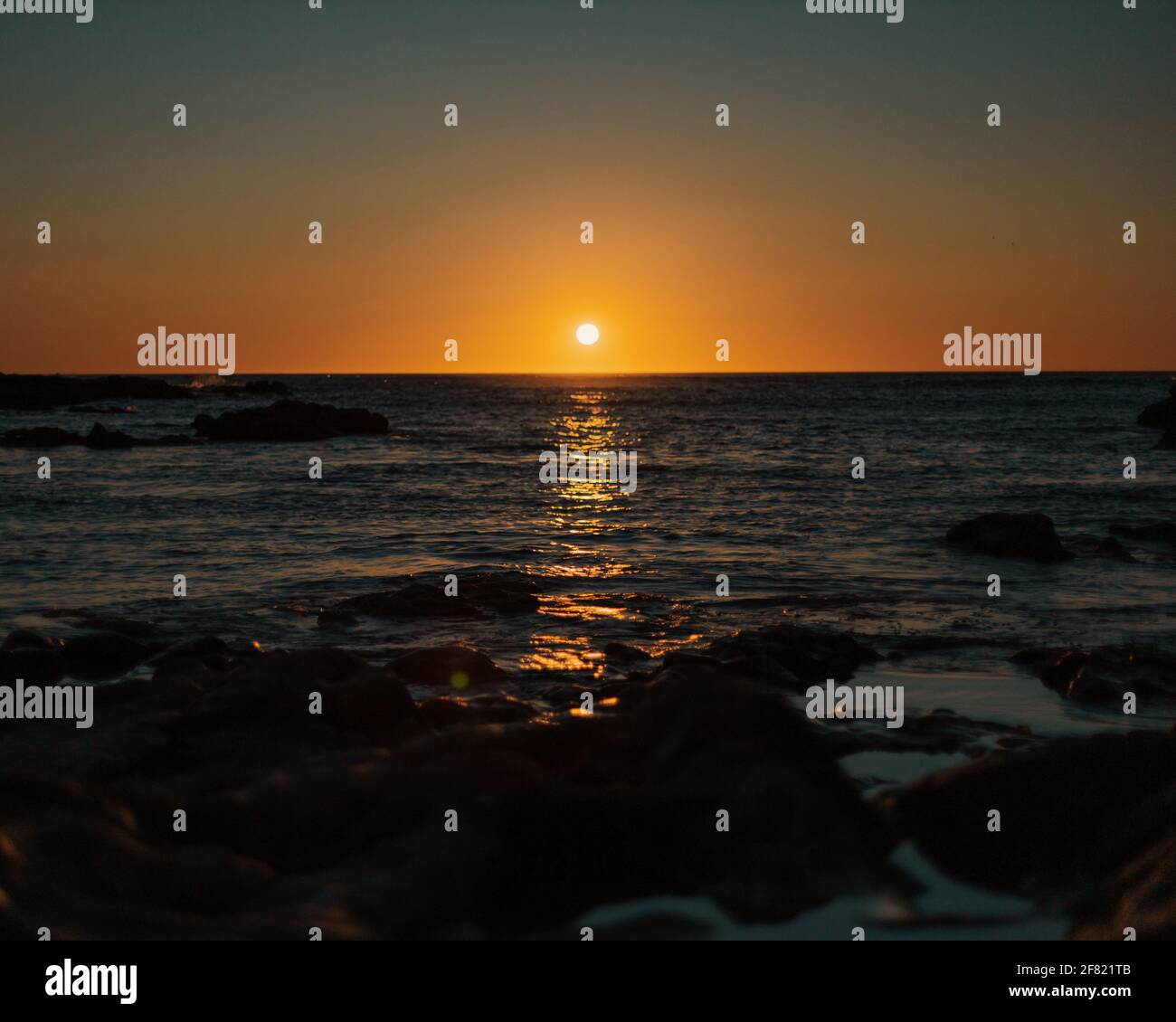 A breathtaking sunset scene with rocky beach and golden sun glazing ...