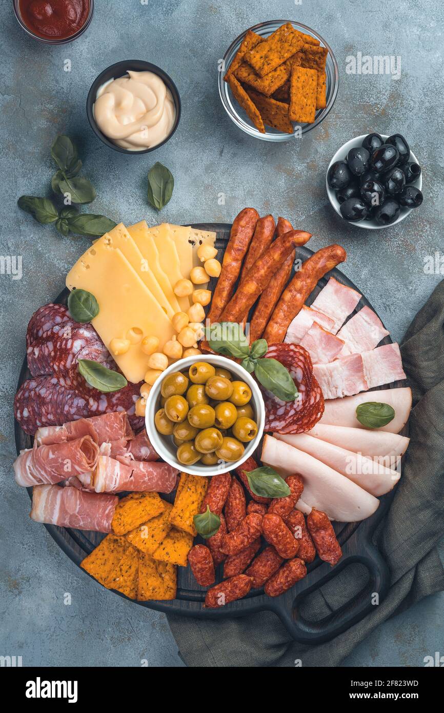 Meat appetizer, assortment of sausage, cheese, olives and basil on a cutting board on a gray