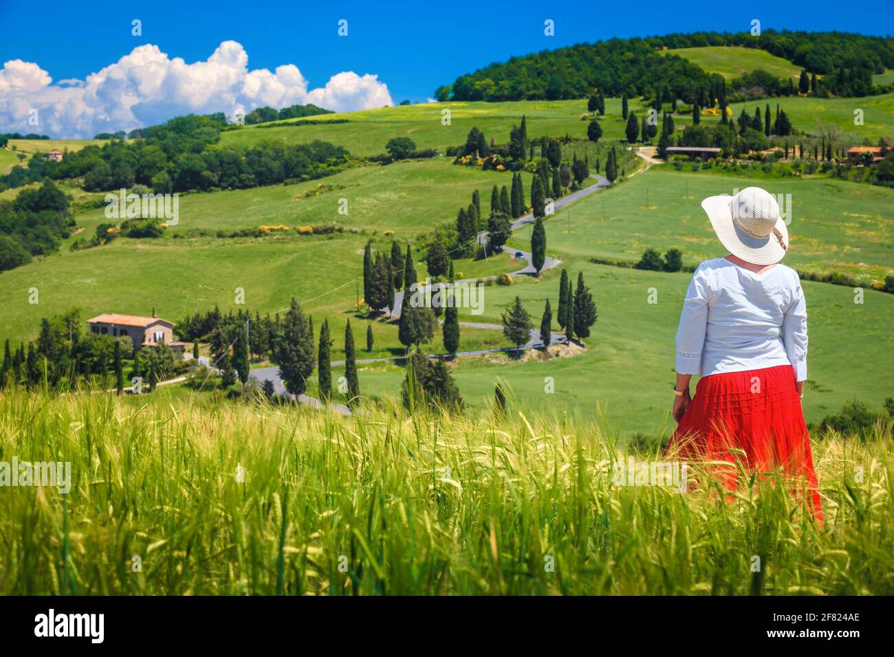 Attractive cheerful woman in a red skirt white shirt and a straw hat enjoying the view in Tuscany. Beautiful rural touristic place with grain fields a Stock Photo