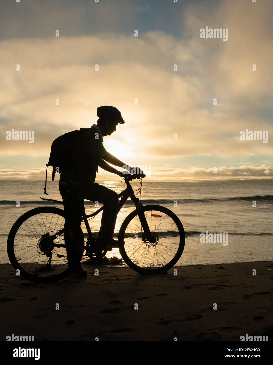 Silhouette image of a cyclist getting ready to ride on the beach at sunrise. Vertical format. Stock Photo