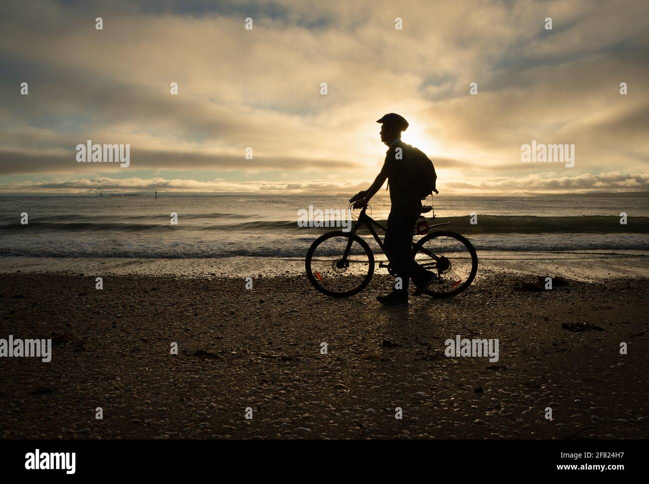 Silhouette image of a cyclist walking and pushing the bike on the beach at sunrise Stock Photo