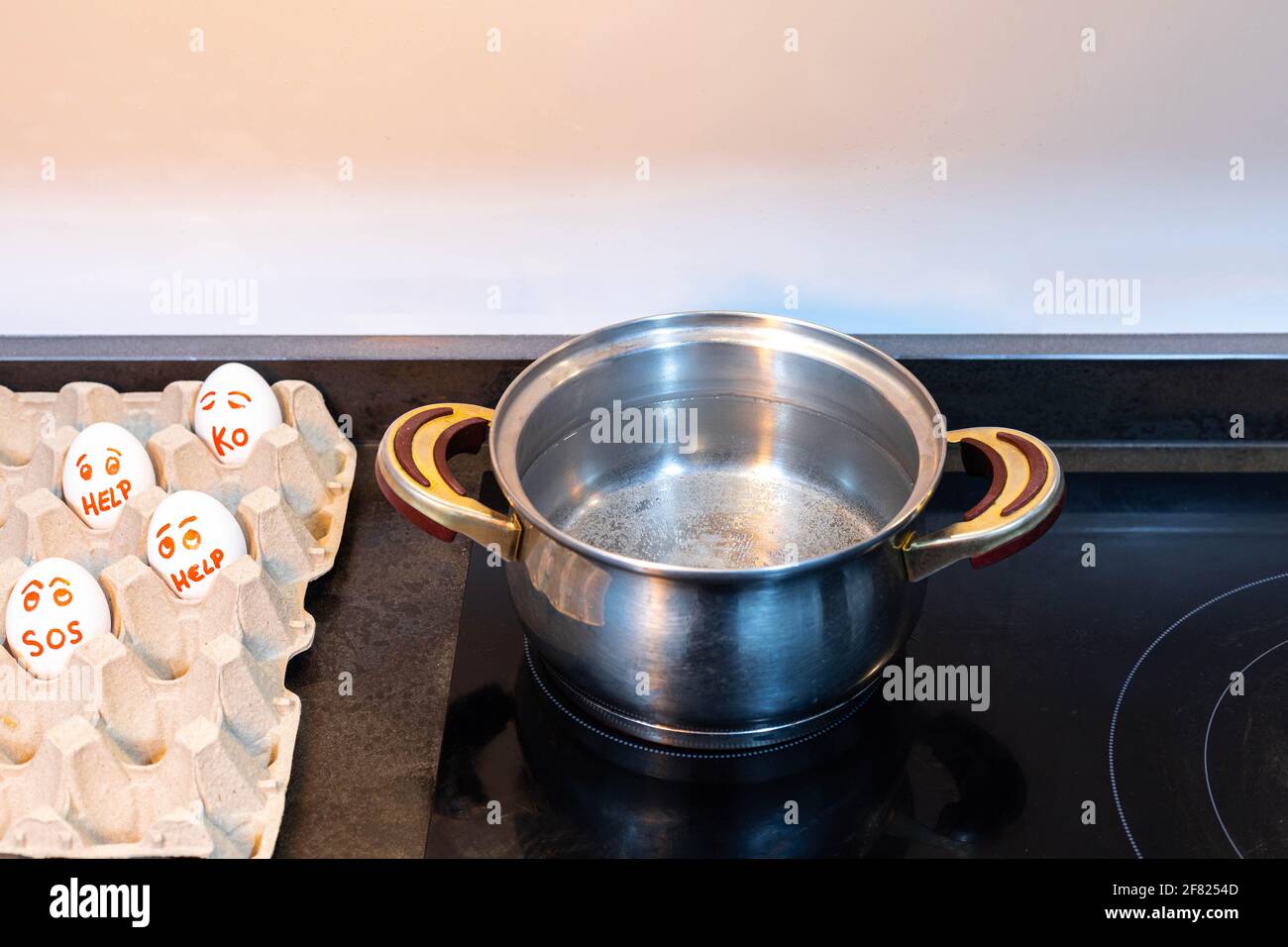 White eggs with eyes asking for help along with a pot of boiling water for cooking concept help Stock Photo