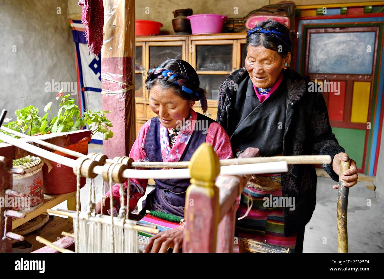 (210411) -- XIGAZE, April 11, 2021 (Xinhua) -- Lhapa (R) teaches her daughter weaving in Puga Village of Xigaze, southwest China's Tibet Autonomous Region, March 20, 2021. Lhapa, born in 1945, is a villager in Puga Village. When she was a child, her mother became blind due to overwork and lost the ability to work. The serf owner drove her out of the manor, and Lhapa's mother had to beg everywhere with her sister for a living. In 1959, during the democratic reform in Tibet, the Lhapa's family were finally reunited and alloted 24 mu (about 1.6 hectare) of land, six sheep and two cows. They al Stock Photo
