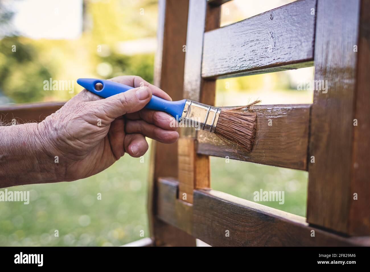 Paint wooden furniture. Renovation of garden chair. Closeup hand with
