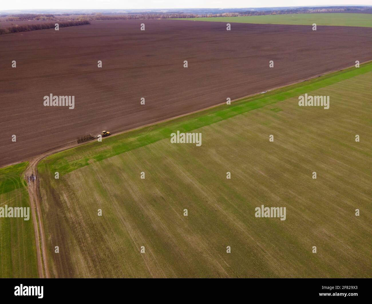 Aerial view of a modern yellow tractor rides across the field, plowing ...