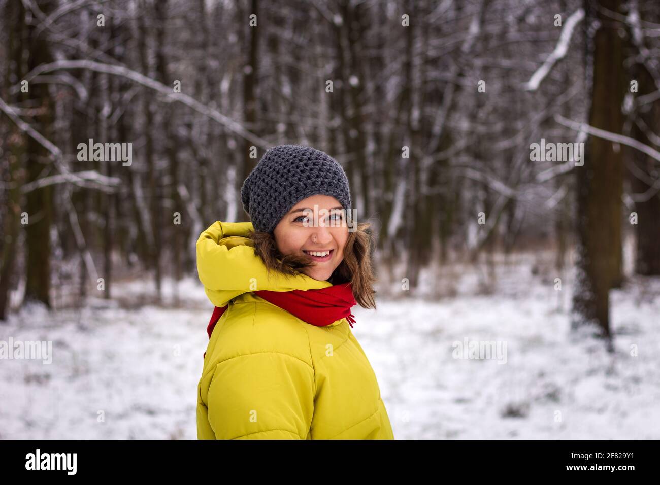 Beautiful young woman wearing winter coat and knit hat in snow forest. Smiling woman walking in winter Stock Photo