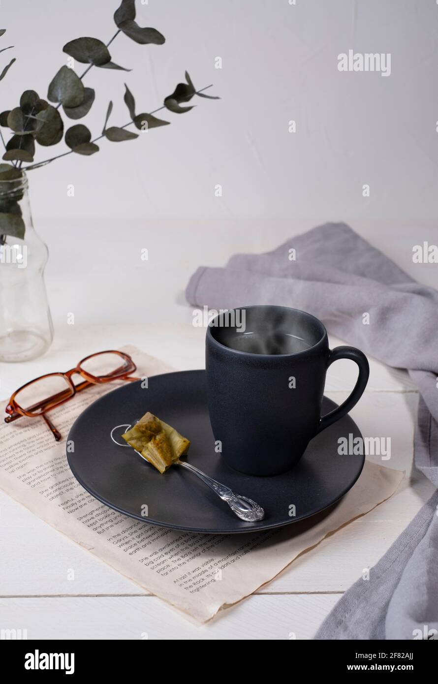 It's teatime, time to relax, black ceramic cup on a saucer with hot steaming tea Stock Photo