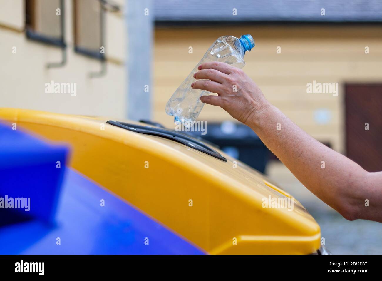 Hand throwing plastic garbage to recycling bin at city street
