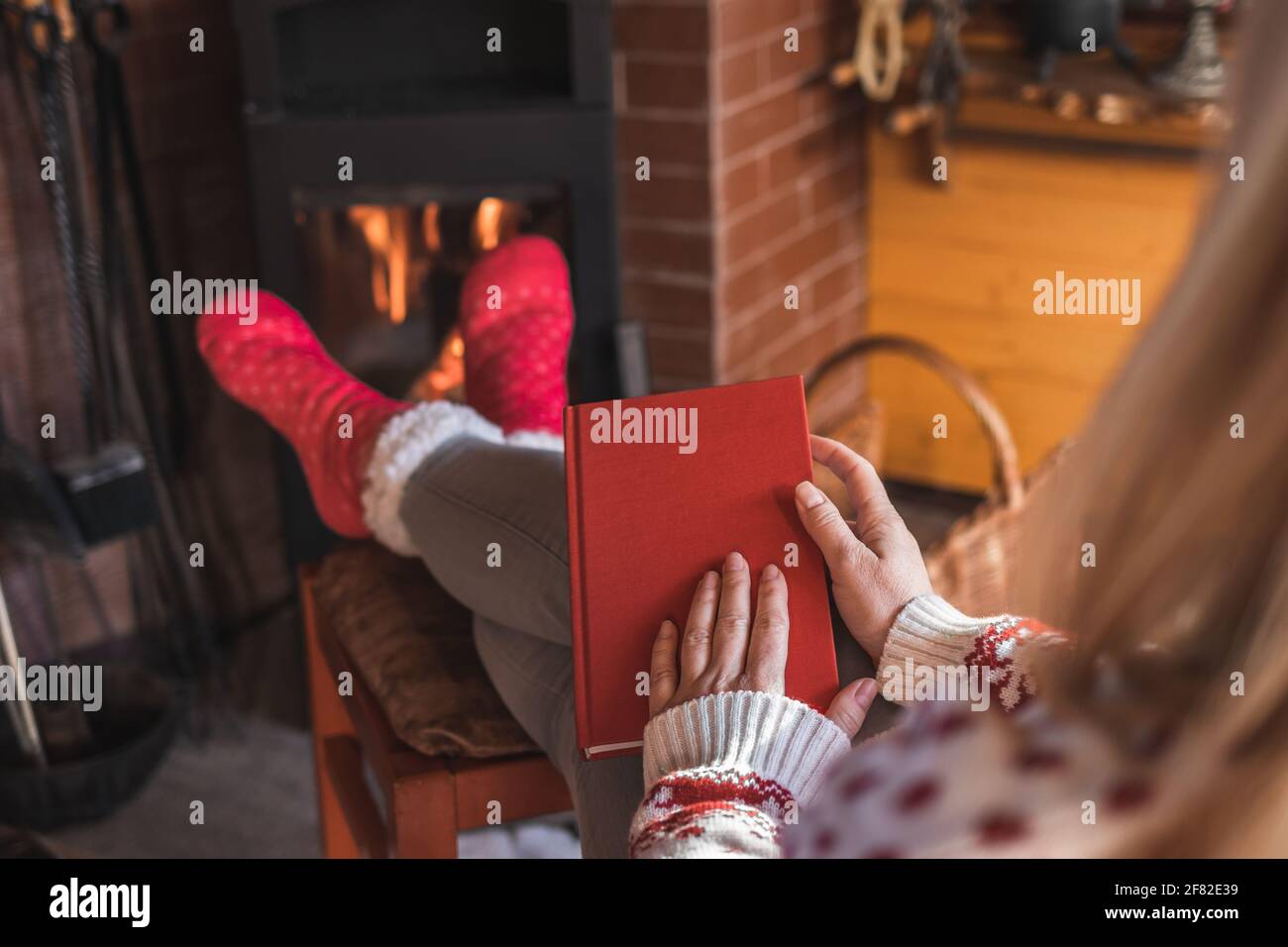 Woman relaxing with book in front of fireplace at home interior. Woman reading book at cozy indoors. Home sweet home Stock Photo