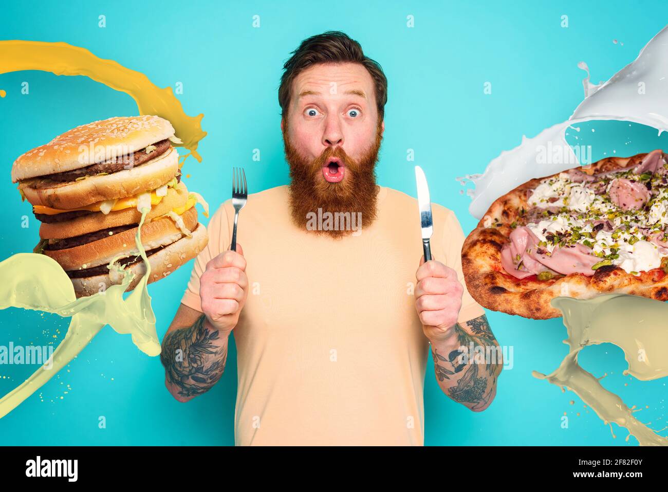 Man with tattoos is ready to eat sandwich and pizza with cutlery in hand. cyan background Stock Photo