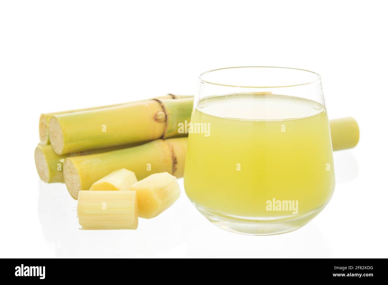 Fresh squeezed sugar cane juice in glass with cut pieces cane isolated