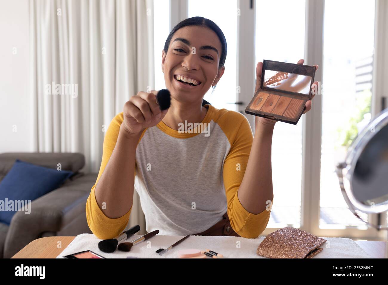 Mixed race gender fluid man making vlog holding foundation powder makeup and brush, smiling Stock Photo