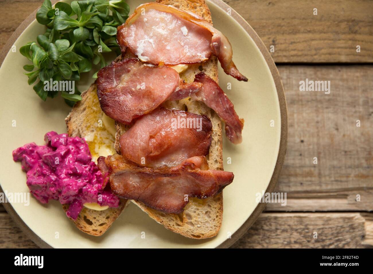 Rashers of smoked back bacon that has been grilled and served on toasted sourdough bread with lambs lettuce and a horseradish and beetroot dressing. T Stock Photo
