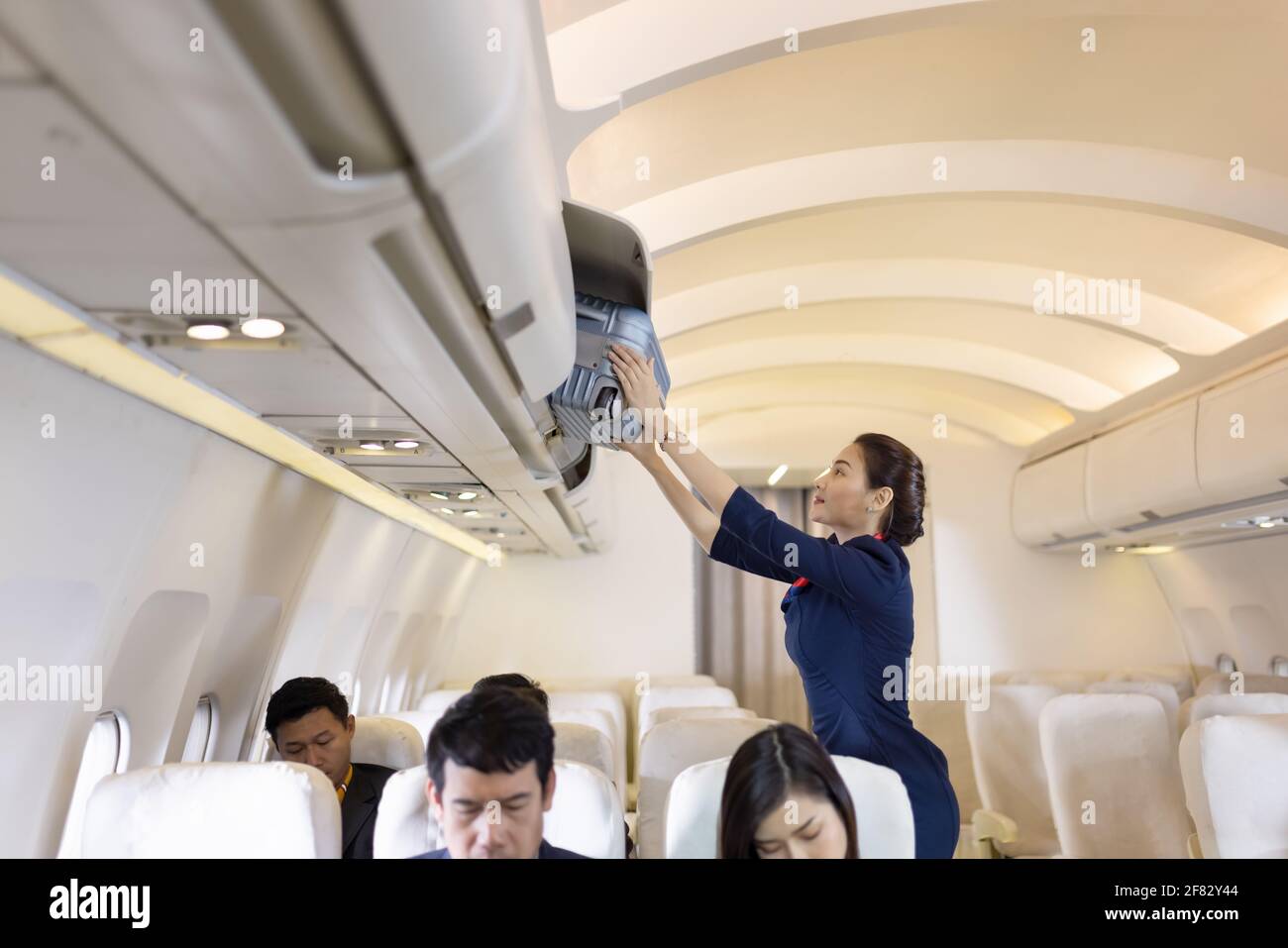The stewardess helps the passengers to put their luggage in the cabin