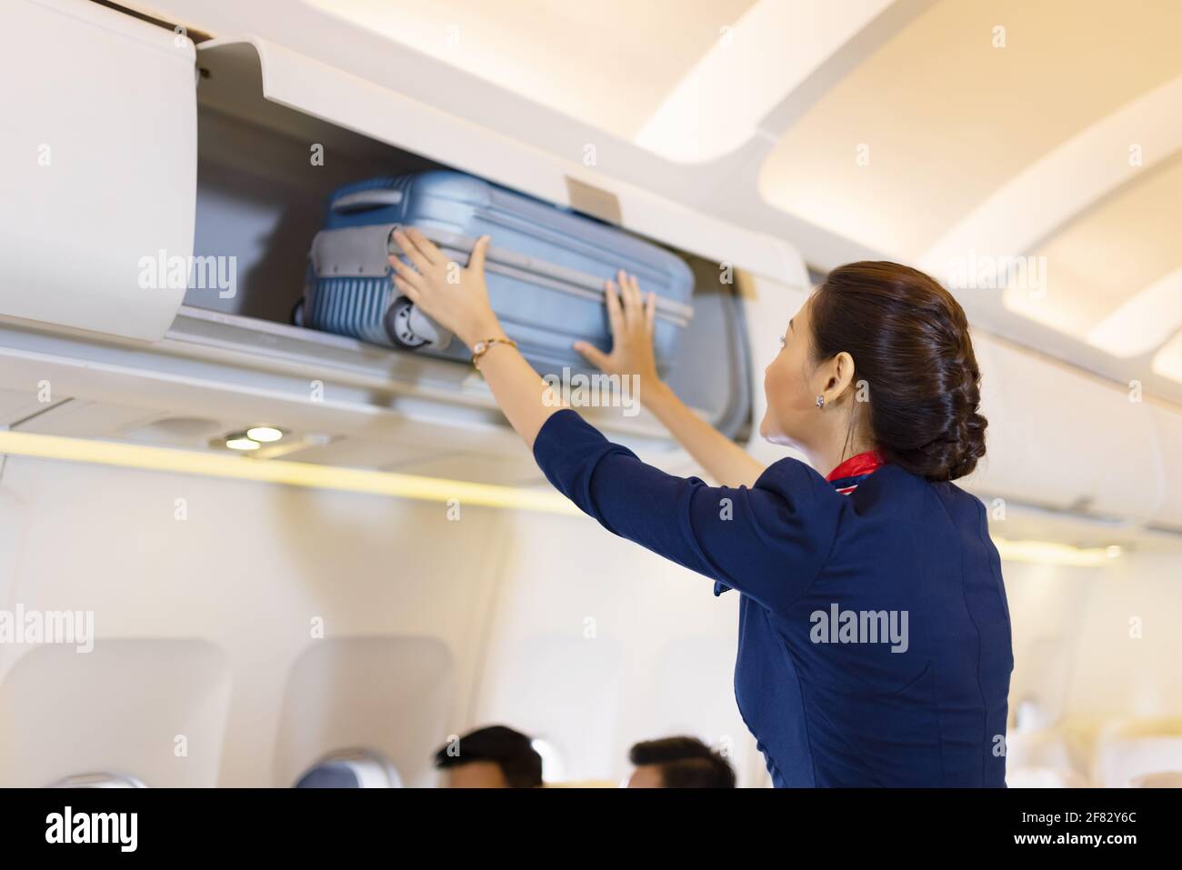 The stewardess helps the passengers to put their luggage in the cabin