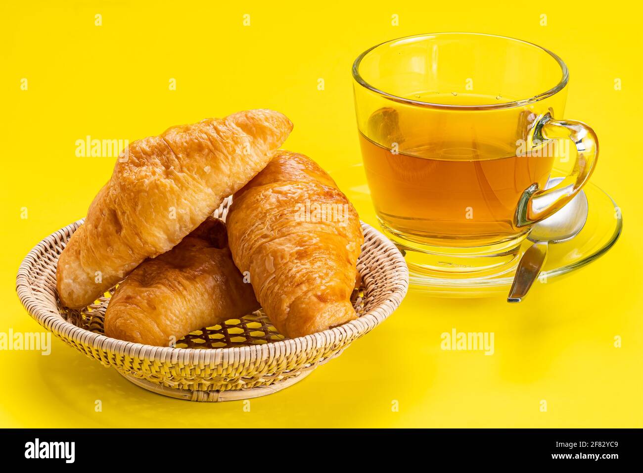 Simply breakfast with homemade croissants on bamboo basket and a cup of hot tea on yellow background. Stock Photo