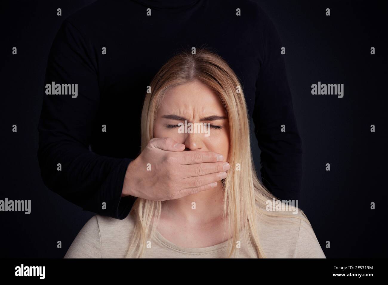 Fear, tyrant, ageism and abused. Male aggressive in black clothes covers mouth with hand of scared young lady Stock Photo
