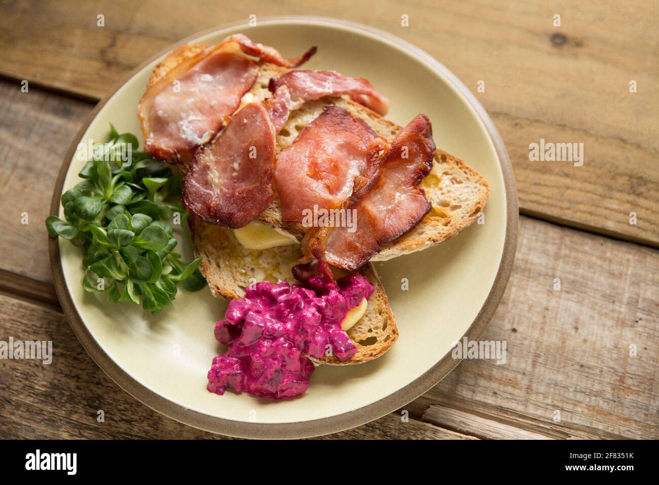 Rashers of smoked back bacon that has been grilled and served on toasted sourdough bread with lambs lettuce and a horseradish and beetroot dressing. T Stock Photo
