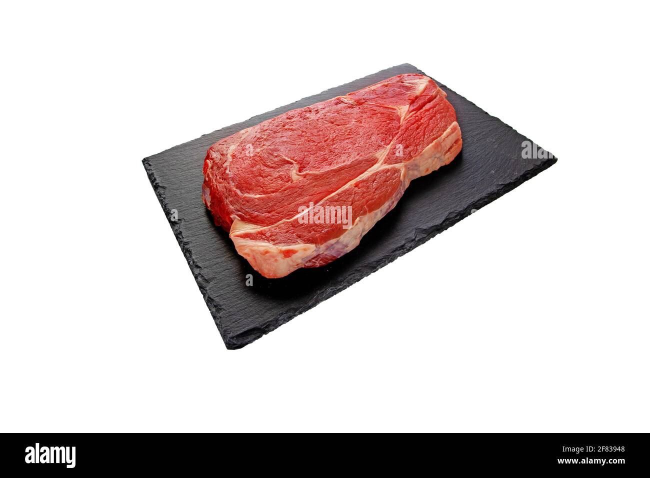 Juicy raw meat cut. Beef entrecote slice on the black textured slate plate isolated on white. Stock Photo