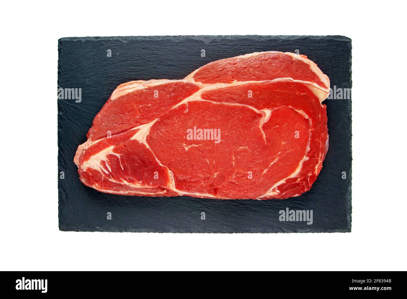 Juicy raw meat cut. Beef entrecote slice on the black textured slate plate isolated on white top view. Stock Photo