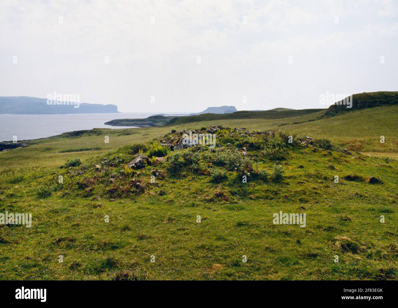 View SW of the remains of Struanmore Neolithic chambered tomb, Bracadale, Isle of Skye, Scotland, UK: Ardtreck Point rear L & Oronsay island rear R. Stock Photo