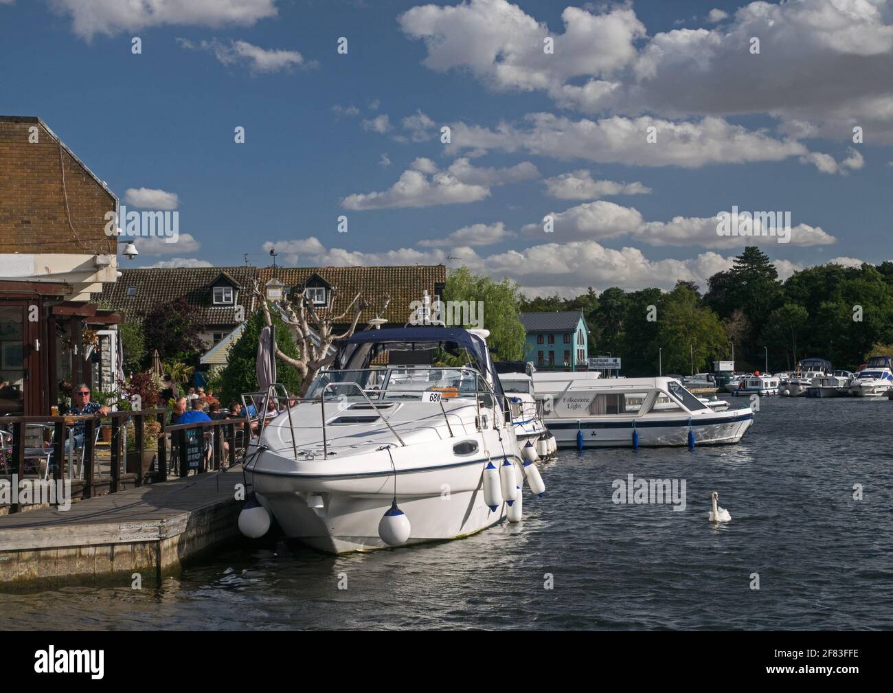 Wroxham on The River Bure with Riverside Alfresco Restaurants & Pubs, alongside moored Yachts, Wroxham, Norfolk, England, UK, Stock Photo
