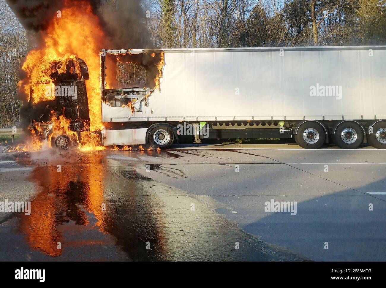 A truck is burning on the highway, with a big fire ball and smoke. Fuel lays on the track, a dangerous situation. Stock Photo