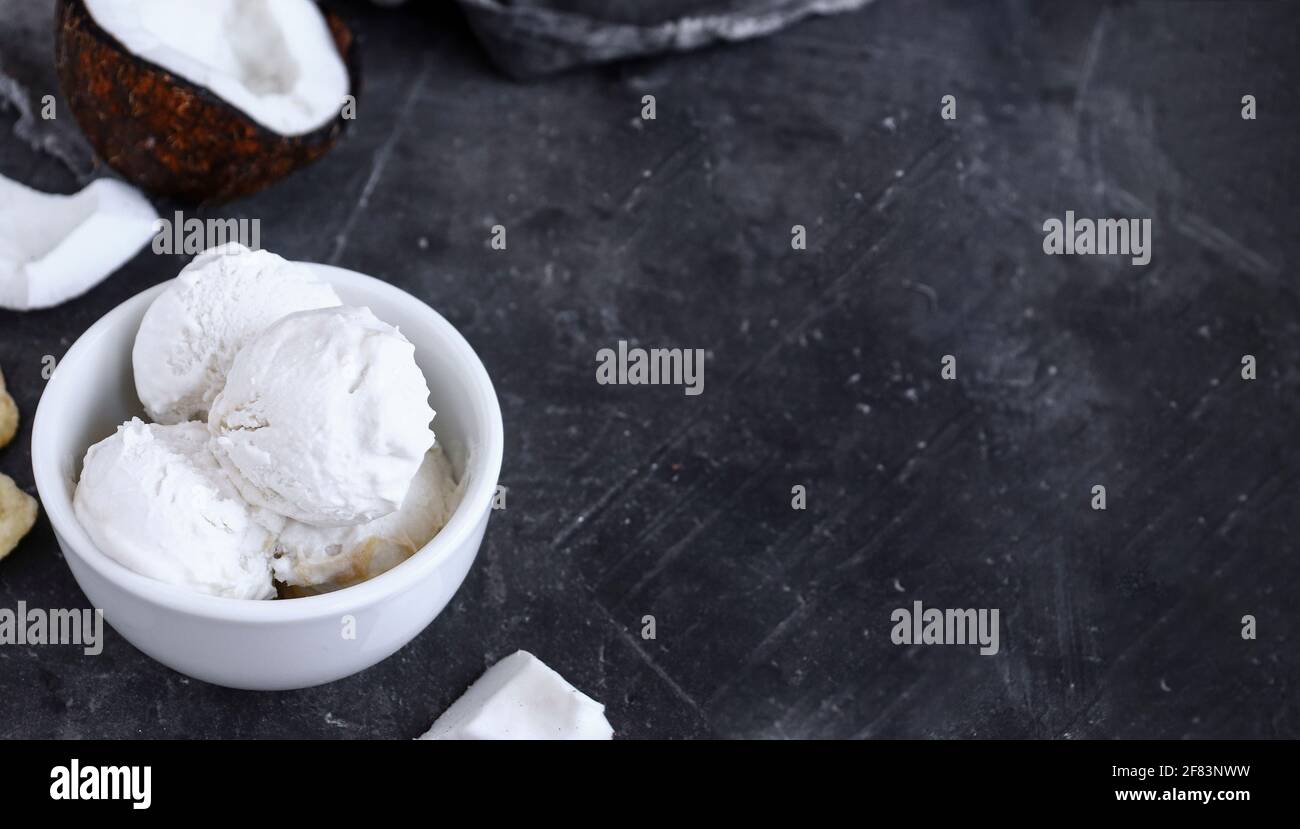 Coconut vegan ice cream in a white cup. Sundae balls. Dark background, copy space. Stock Photo