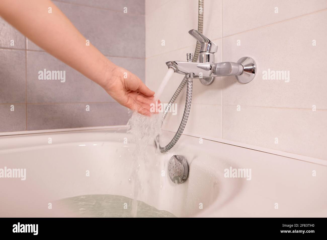 Woman take bath at home checking temperature touching running water