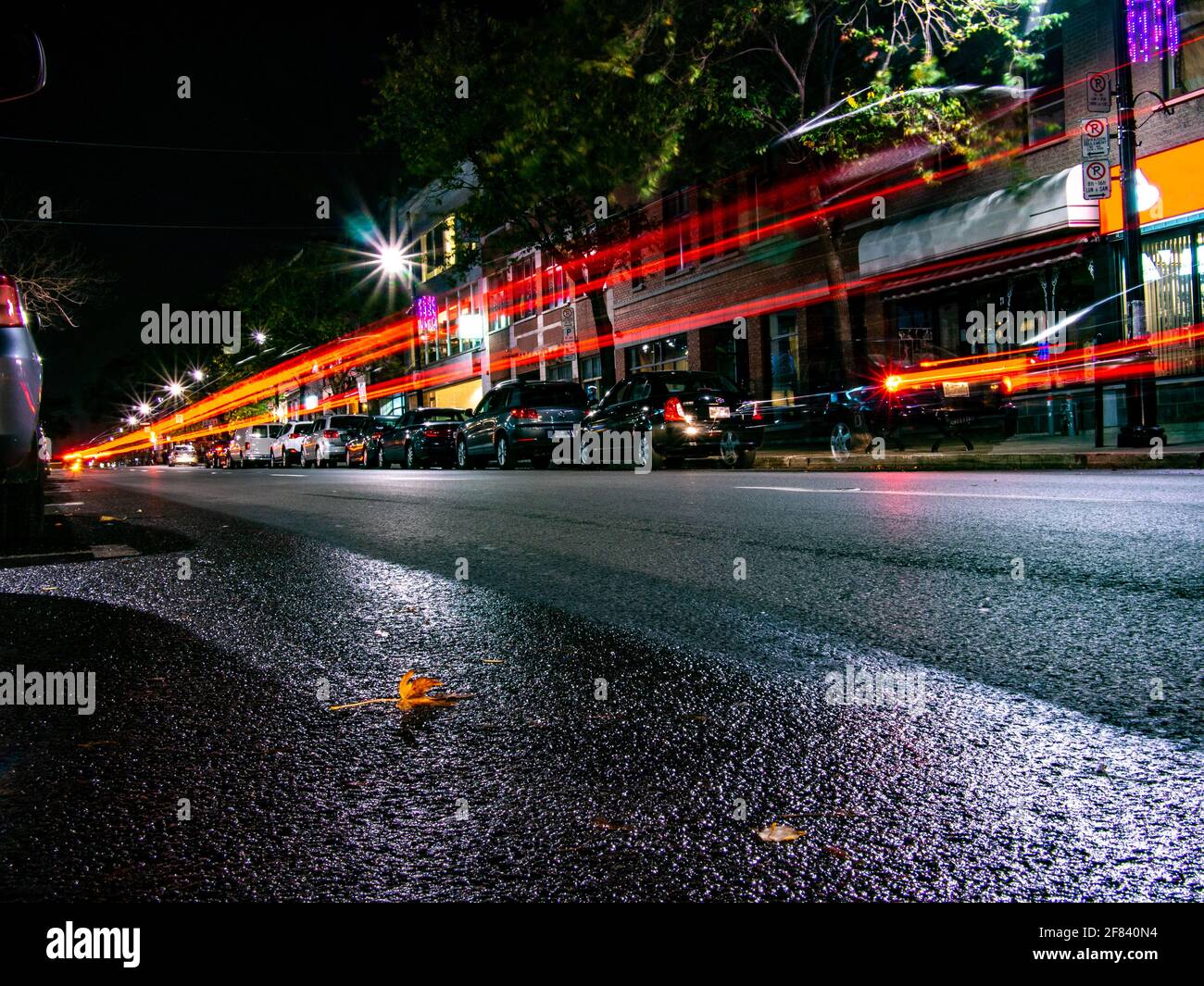 Red rear lights trails from a car passing by at night in a city Stock Photo