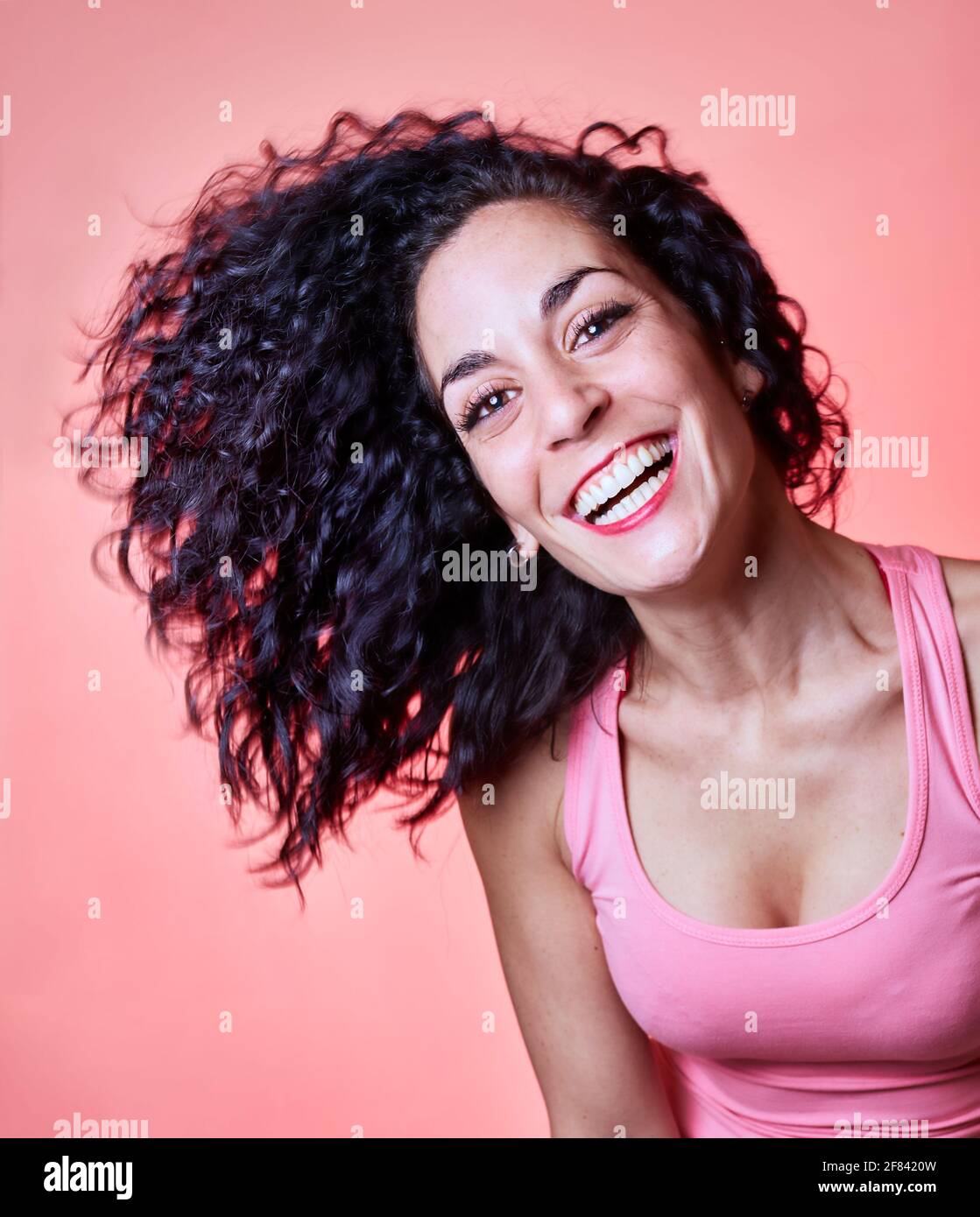 Young black curly haired woman laughing with her long hair to the side looking at camera on a pink background. curly girl method. hair care and beauty Stock Photo