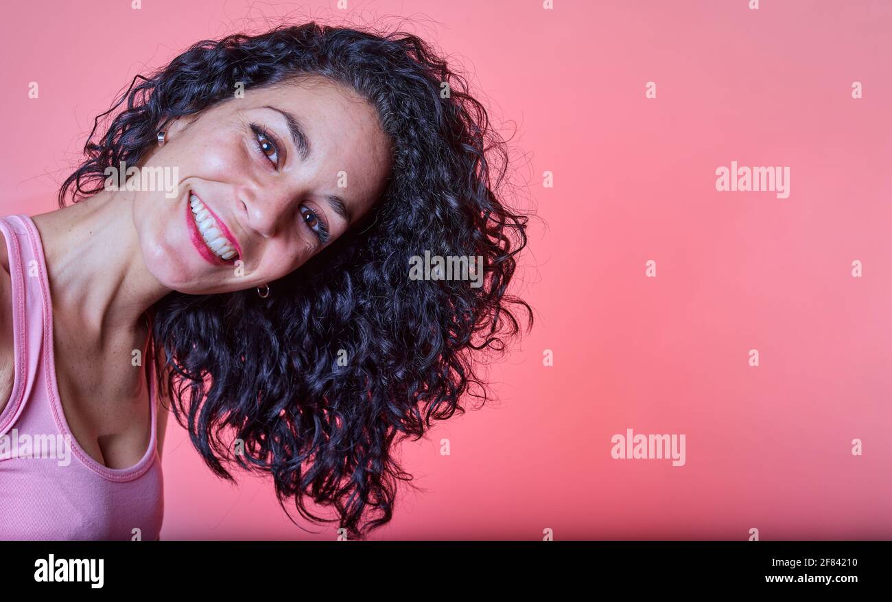 portrait of a young black curly haired woman smiling with her long hair to the side looking at camera on a pink background. curly girl method. hair ca Stock Photo