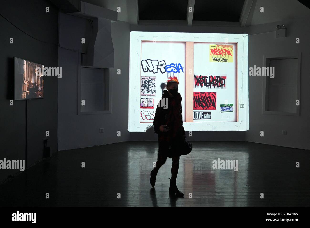 A woman walks past a projection of a NFT, or non-fungible token, high  resolution short video work of art at the Superchief NFT Gallery in New  York, NY, April 10, 2021. The
